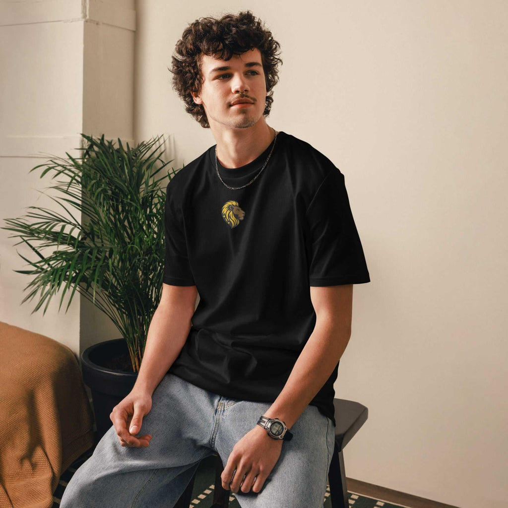 Young man wearing black He Is Risen T-Shirt with gold lion and cross design sitting indoors